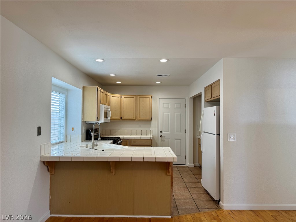 73 Sea Holly Way Henderson, NV 89074 - Photo 49 of 59 Kitchen with tile countertops, a kitchen breakfast bar, a peninsula, freestanding refrigerator, and light wood-style flooring