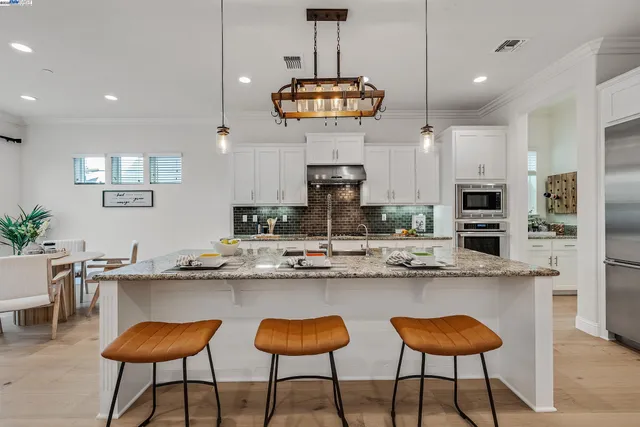 a kitchen with stainless steel appliances kitchen island granite countertop a stove a sink a refrigerator and white cabinets with wooden floor