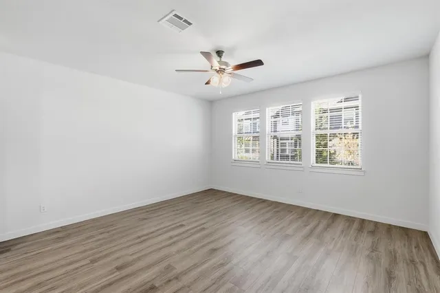an empty room with wooden floor ceiling fan and windows