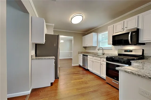 a kitchen with stainless steel appliances a stove top oven a sink a refrigerator white cabinets and wooden floor