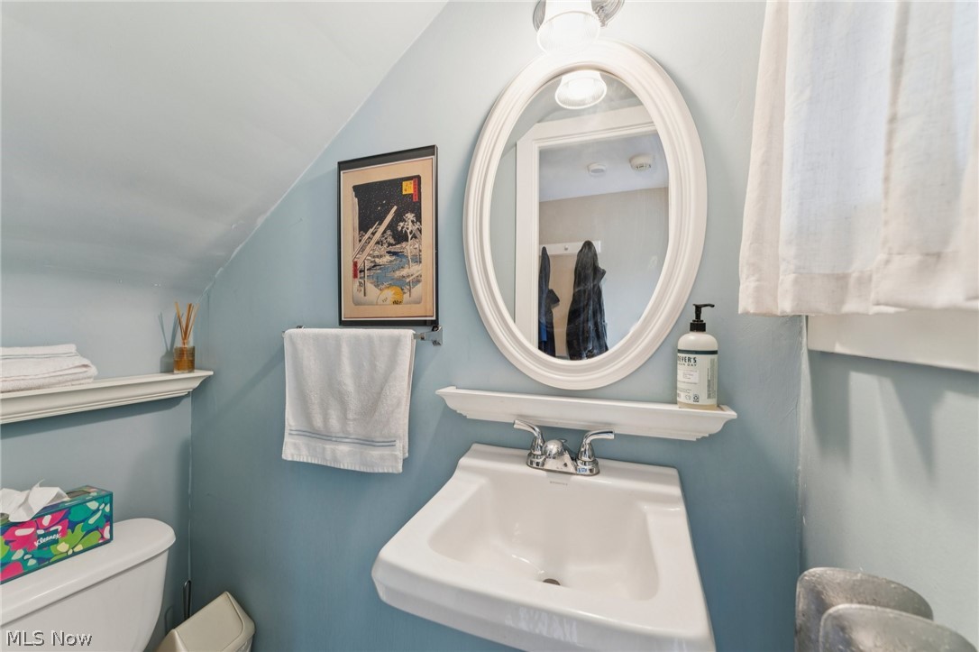 2925 East Overlook Road Cleveland Heights, OH 44118 - Photo 18 of 48 The bathroom features a wall-mounted sink with a chrome faucet, a white framed oval mirror, and a window with white curtains