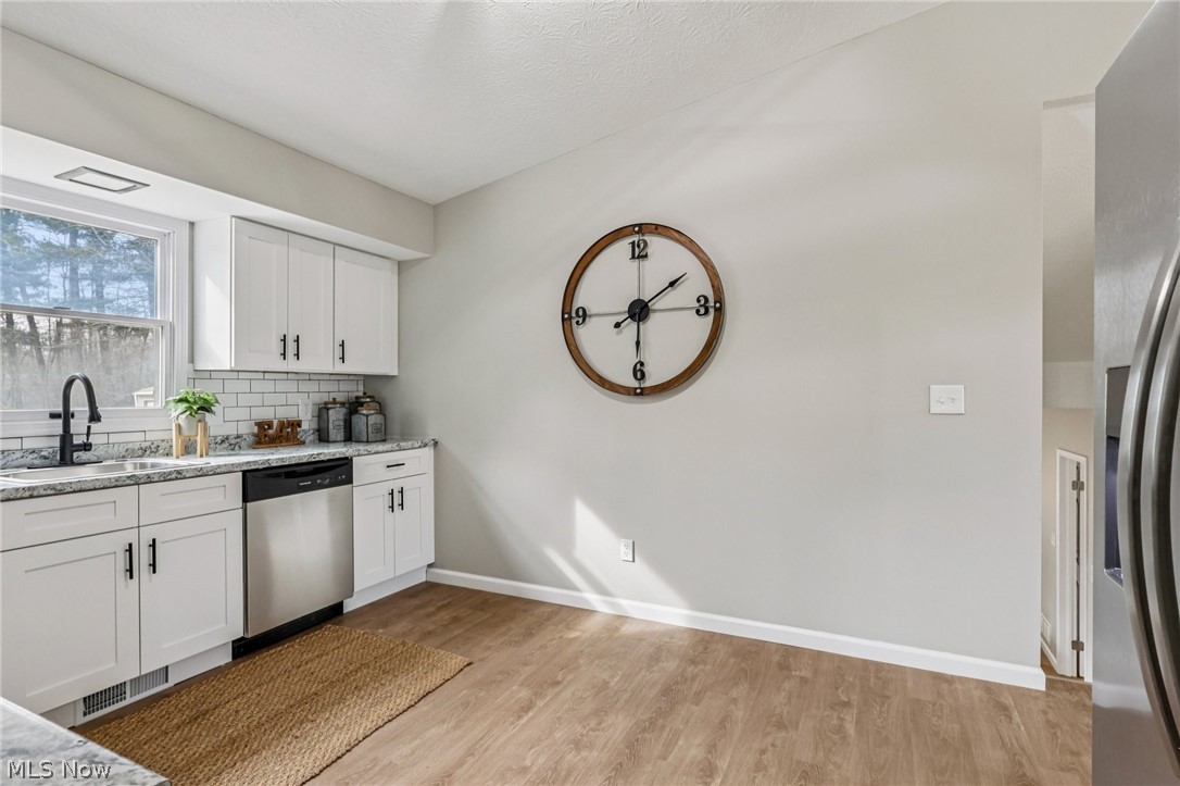 Kitchen featuring white cabinetry, stainless steel appliances, light stone countertops, light wood-style floors, and backsplash