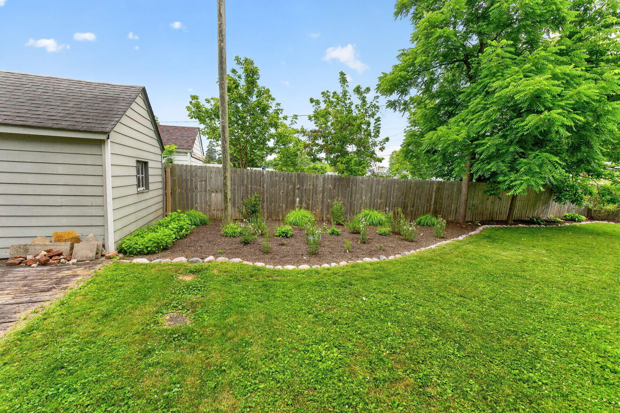 492 Wetmore Road Columbus, OH 43214 - Photo 45 of 55 Expansive green lawn with a curved garden bed, bordered by a wooden privacy fence and mature trees