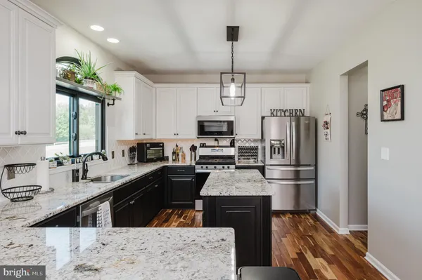 a kitchen with stainless steel appliances kitchen island granite countertop a refrigerator a sink dishwasher a stove and white cabinets with wooden floor