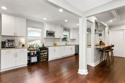 a kitchen with stainless steel appliances kitchen island granite countertop a stove a sink a refrigerator and white cabinets with wooden floor