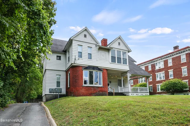 a view of a brick house with a big yard and large trees