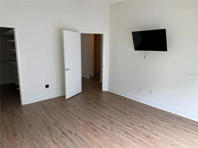 a view of an empty room with wooden floor and fan