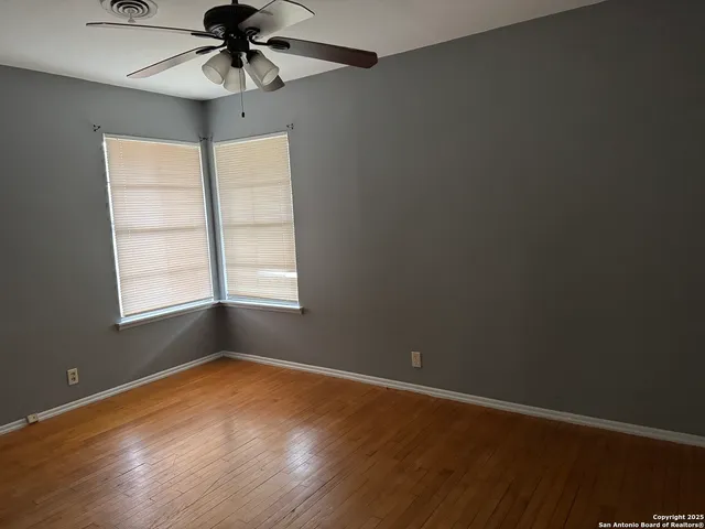 an empty room with wooden floor chandelier fan and windows