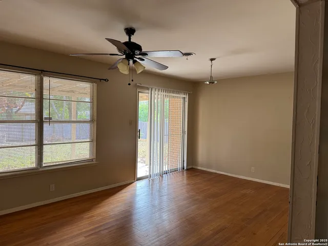 an empty room with wooden floor fan and windows