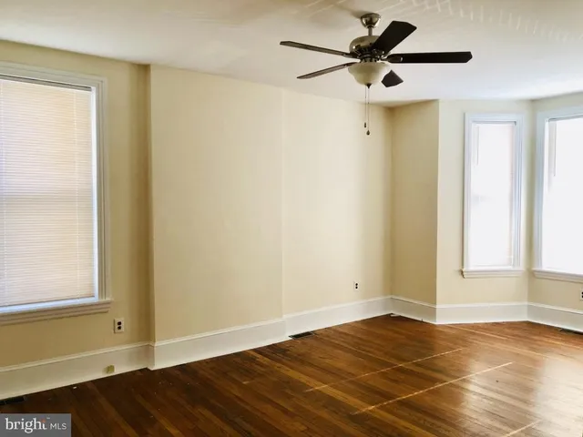 a view of empty room with wooden floor and fan