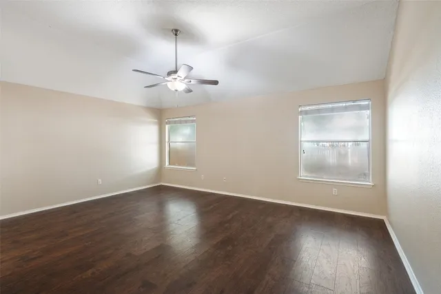 an empty room with wooden floor chandelier fan and windows