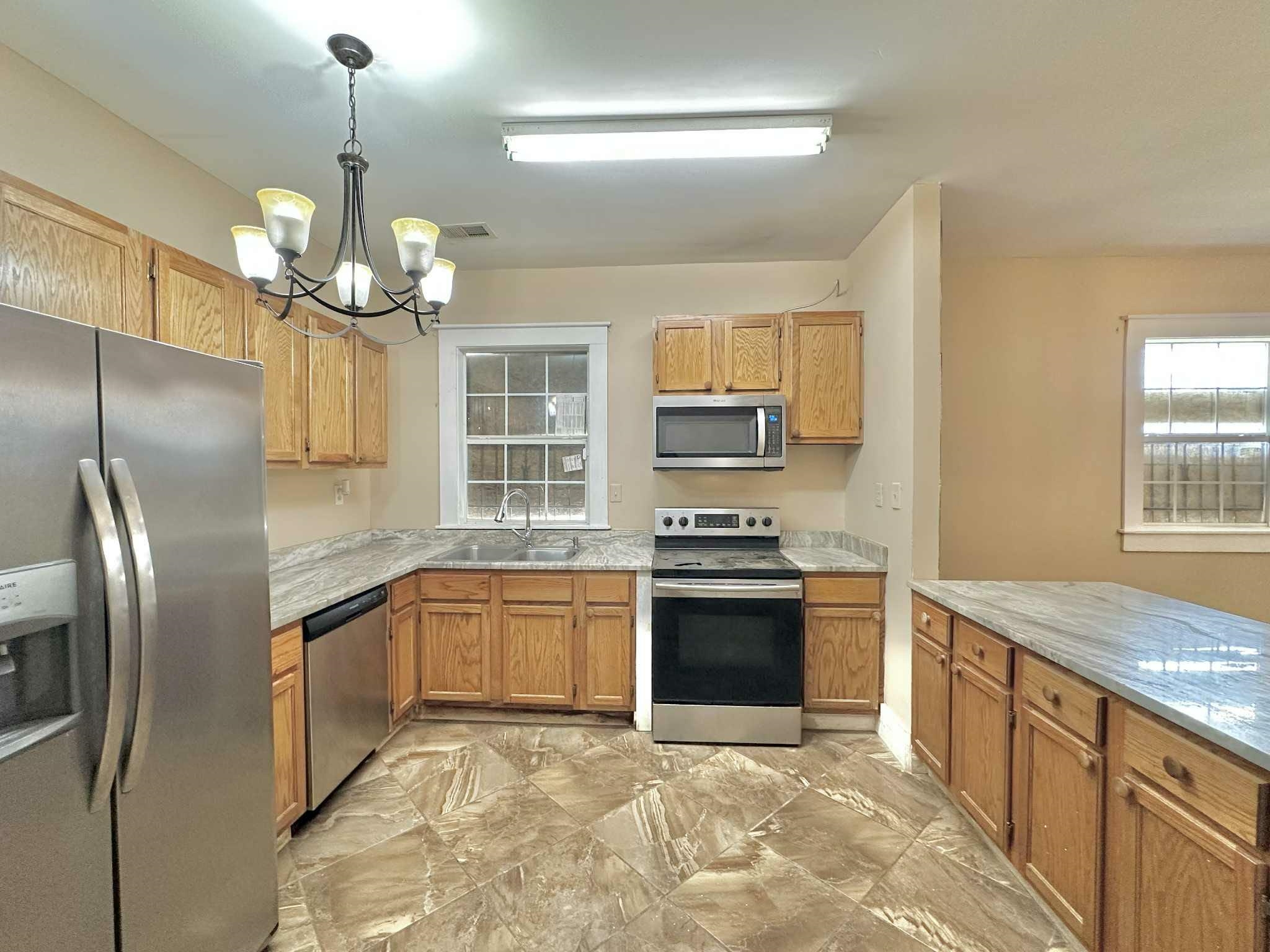 896 Orphanage Avenue Memphis, TN 38107 - Photo 8 of 17 Kitchen with stainless steel appliances, hanging light fixtures, a chandelier, light marble finish flooring, and brown cabinetry