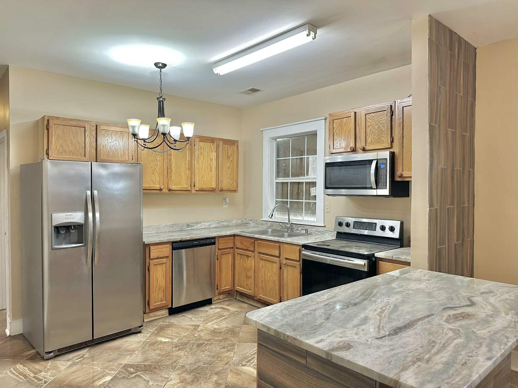 896 Orphanage Avenue Memphis, TN 38107 - Photo 9 of 17 Kitchen featuring stainless steel appliances, hanging light fixtures, a chandelier, and brown cabinetry