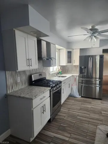 a kitchen with stainless steel appliances granite countertop a stove a sink dishwasher a refrigerator and white cabinets with wooden floor