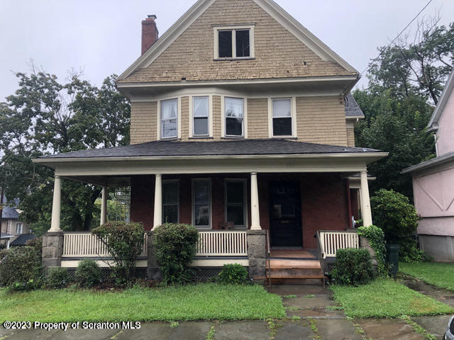a view of brick house with a yard plants and large tree
