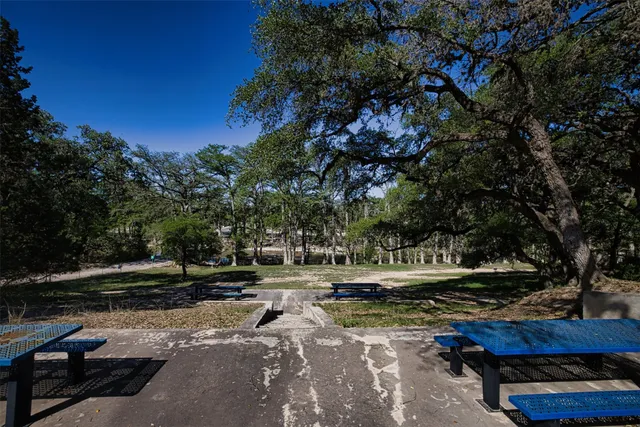 a view of a patio with table and chairs under an umbrella with large trees