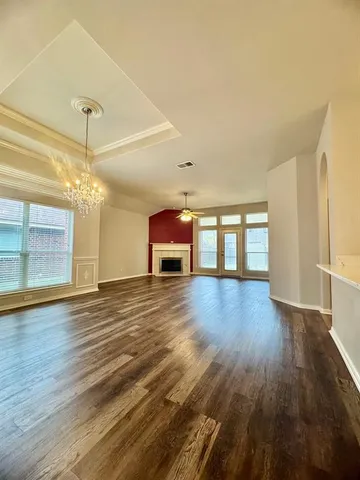 an empty room with wooden floor chandelier and windows