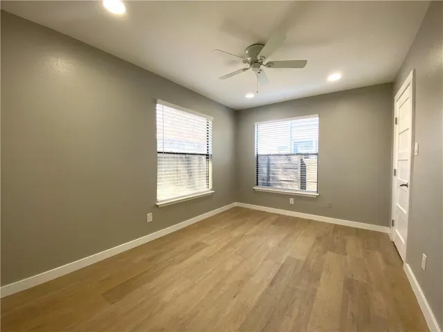 an empty room with wooden floor fan and windows