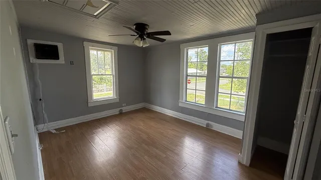 an empty room with wooden floor a ceiling fan and windows
