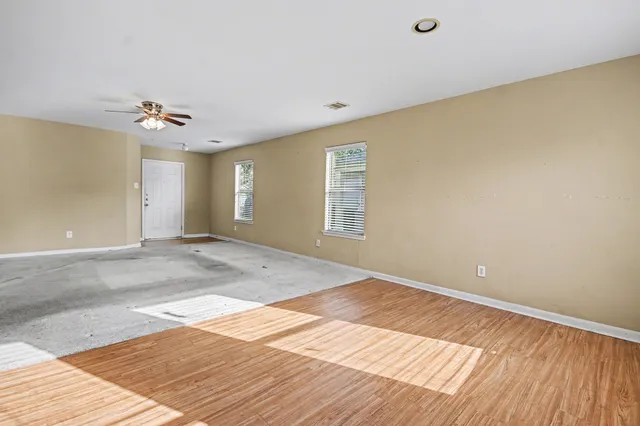 a view of an empty room with window and chandelier fan