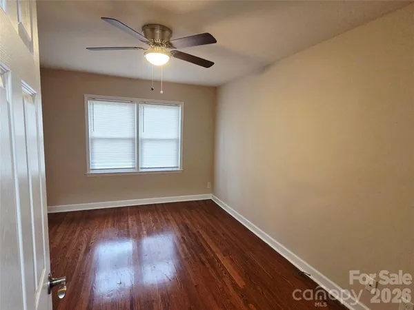 an empty room with wooden floor chandelier fan and windows