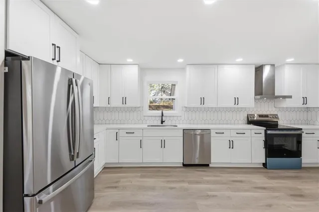 a kitchen with stainless steel appliances a refrigerator a stove a sink and white cabinets