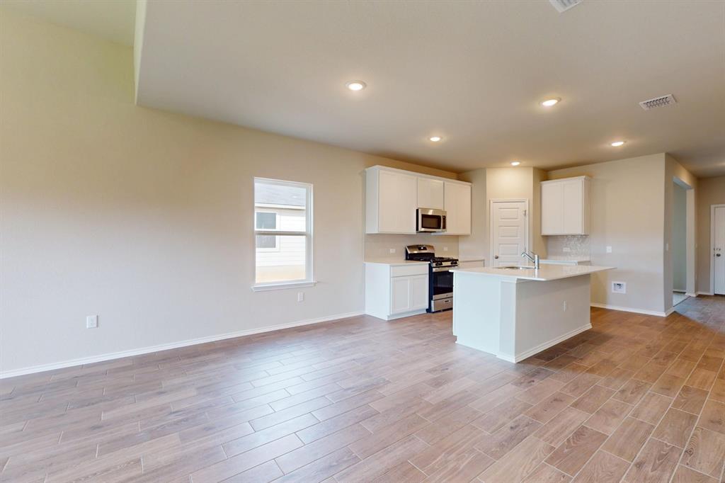 4509 Beacon Bay Drive Austin, TX 78747 - Photo 29 of 30 Kitchen with stainless steel appliances, white cabinets, wood finish floors, a kitchen island with sink, and open floor plan