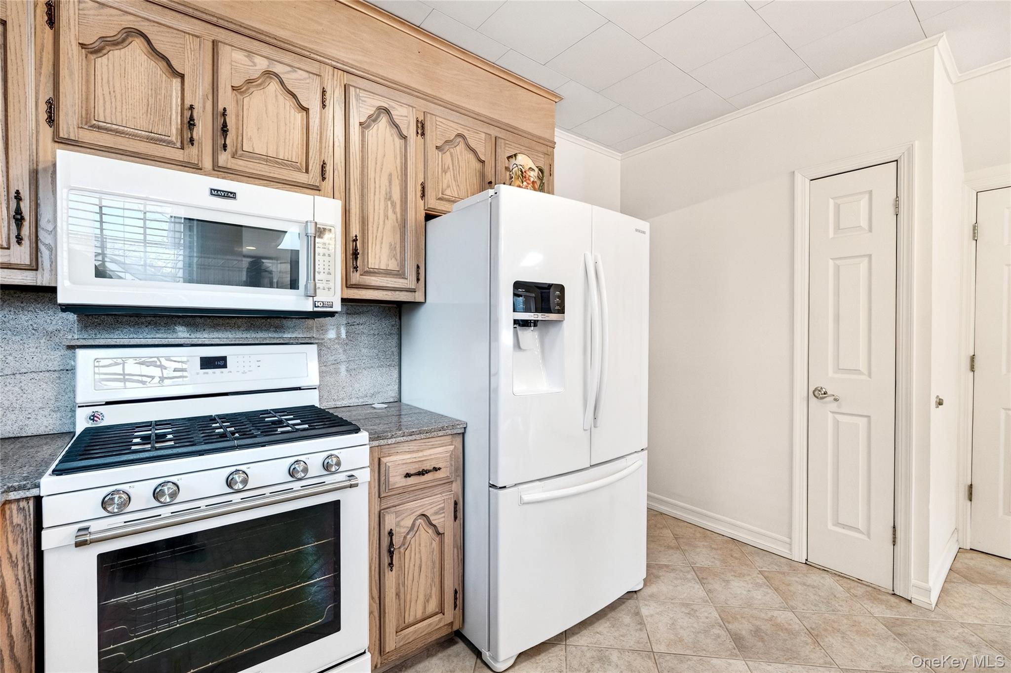 3334 Country Club Road Bronx, NY 10465 - Photo 20 of 49 Kitchen featuring white appliances, ornamental molding, backsplash, dark stone countertops, and light brown cabinetry