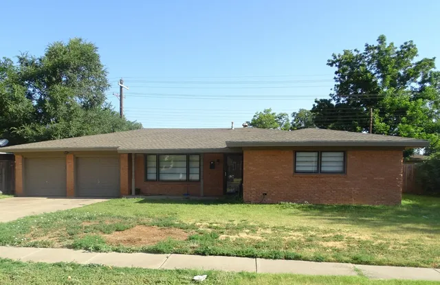 a view of a house with a yard plants and large tree