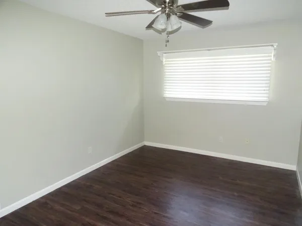 an empty room with wooden floor fan and windows