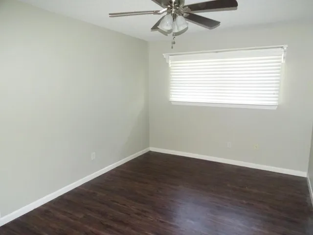 an empty room with wooden floor fan and windows