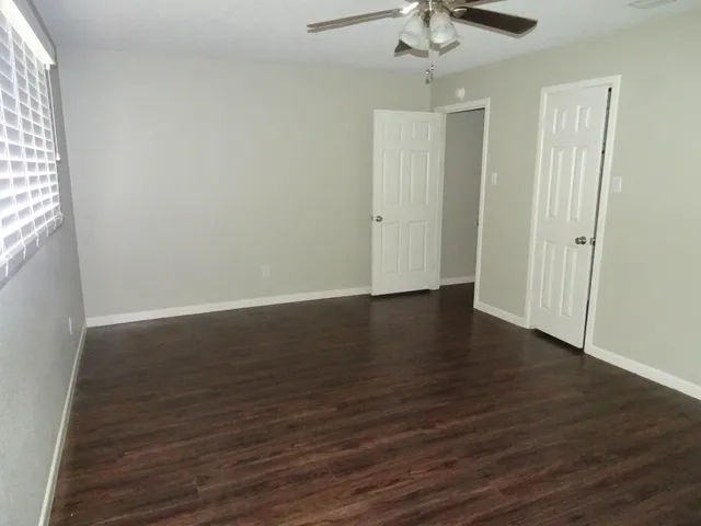 an empty room with wooden floor fan and windows