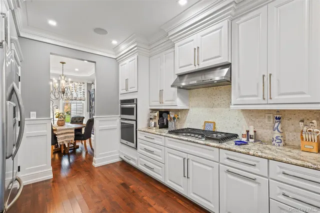 a kitchen with stainless steel appliances granite countertop a stove a sink dishwasher and white cabinets with wooden floor