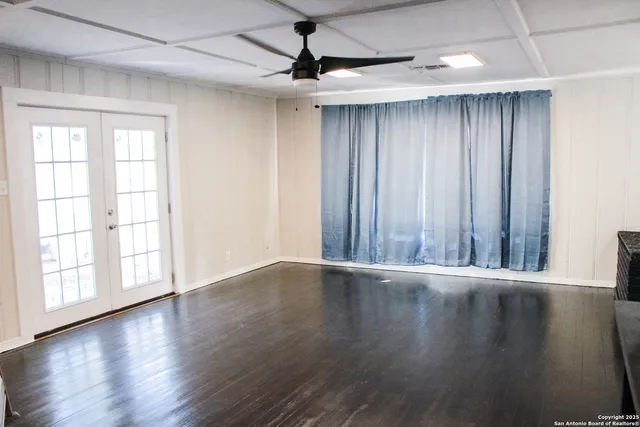 an empty room with wooden floor chandelier fan and windows