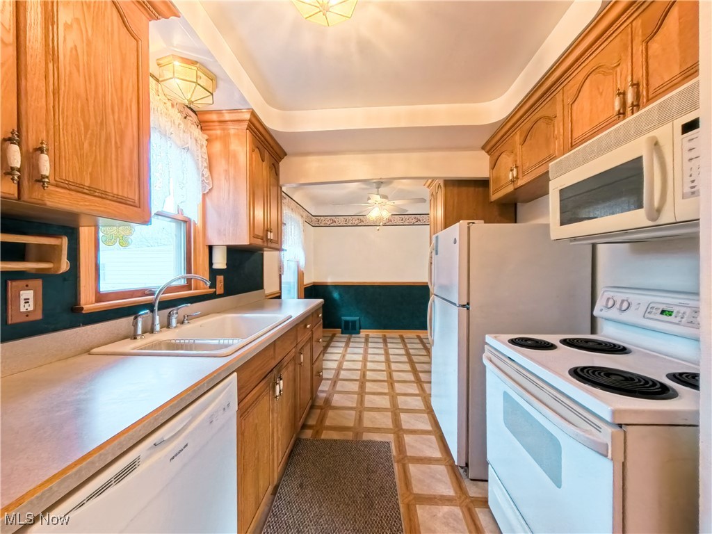 1668 Harwich Road Cleveland, OH 44124 - Photo 4 of 19 Kitchen with white appliances, a wainscoted wall, light countertops, brown cabinets, and ceiling fan