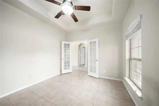 an empty room with chandelier fan and windows