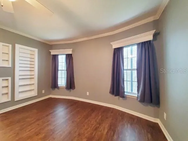 an empty room with wooden floor and windows with curtains