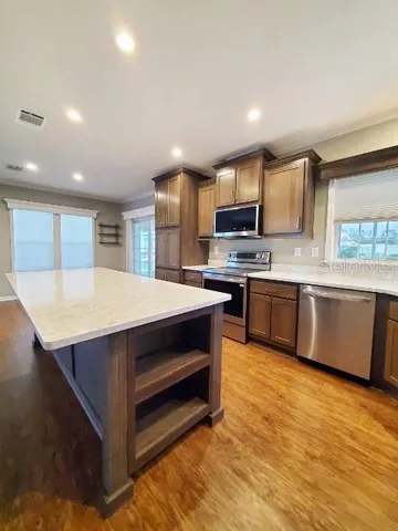 a kitchen with stainless steel appliances kitchen island granite countertop a stove top oven a sink dishwasher a dining table and chairs with wooden floor