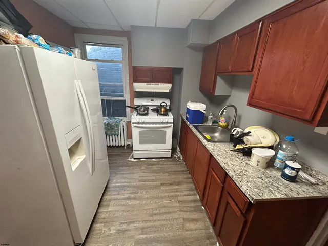 a kitchen with granite countertop a refrigerator a sink a stove and wooden cabinets