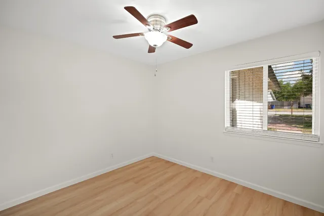 an empty room with wooden floor fan and windows