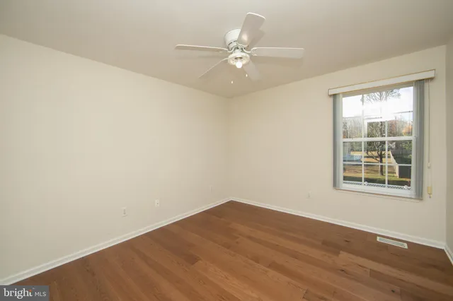 an empty room with wooden floor fan and windows