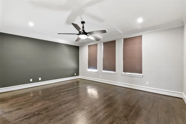 a view of an empty room with wooden floor and a ceiling fan