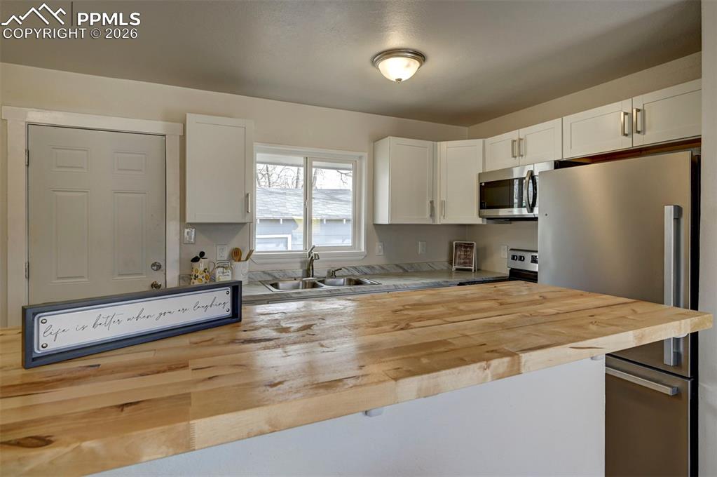 701 Erie Road Colorado Springs, CO 80910 - Photo 12 of 27 a kitchen with stainless steel appliances granite countertop a sink a stove a refrigerator a window with white cabinets and wooden floor