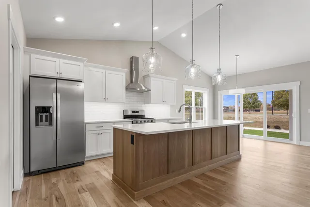 a kitchen with stainless steel appliances granite countertop a sink a stove a refrigerator and island with wooden floor