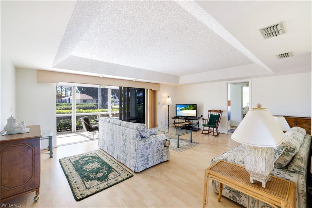 247 Winners Circle, Unit 5 Naples, FL 34112 - Photo 5 of 24 Living room with a raised ceiling, light wood-style floors, and a textured ceiling