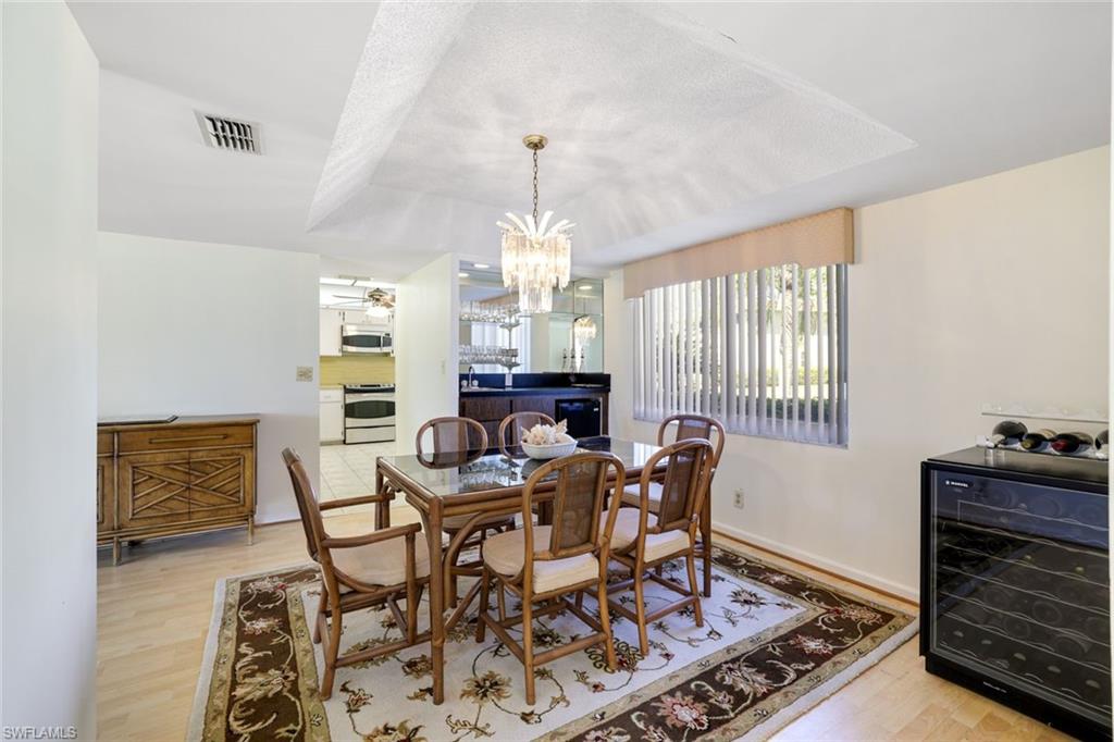 247 Winners Circle, Unit 5 Naples, FL 34112 - Photo 8 of 24 Dining space featuring wine cooler, light wood-style flooring, a chandelier, and a tray ceiling
