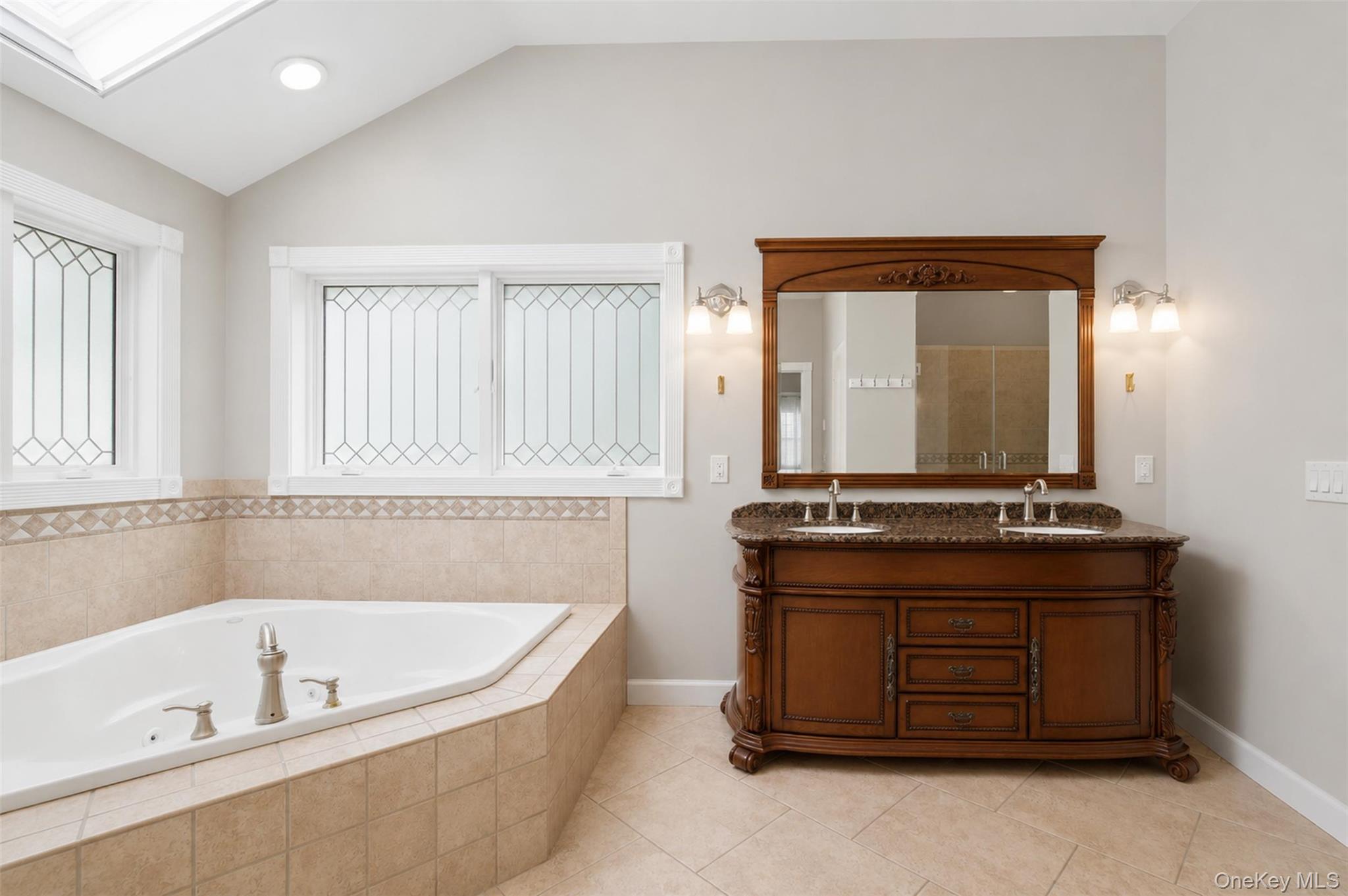 12 Leeside Road Carmel, NY 10512 - Photo 18 of 44 Soaking jet tub with tiled surround, dual-sink vanity with stone countertop, decorative windows, and vaulted ceiling with recessed lighting and skylight