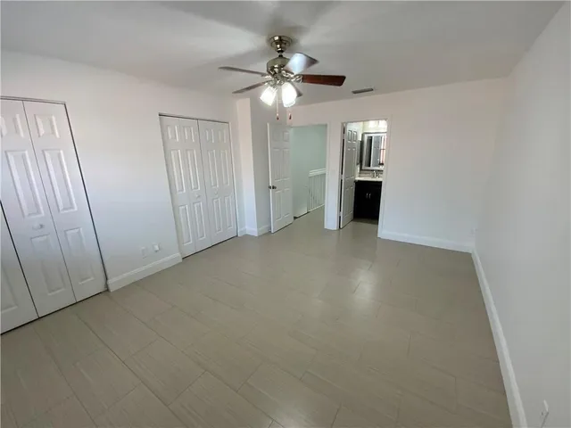 an empty room with chandelier fan and windows