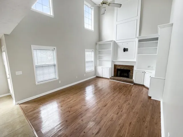 an empty room with wooden floor fireplace and windows