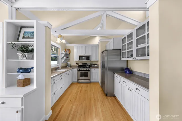 a kitchen with stainless steel appliances granite countertop a refrigerator a sink dishwasher a stove and white cabinets with wooden floor